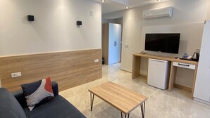 A modern living room with a sofa, a coffee table, a TV, and a kitchenette area. - The Brothers Suite (Dalaman)