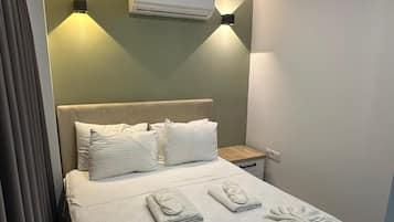 Habitación de hotel con cama, almohadas, mesita de noche, aire acondicionado y lámpara de pared.