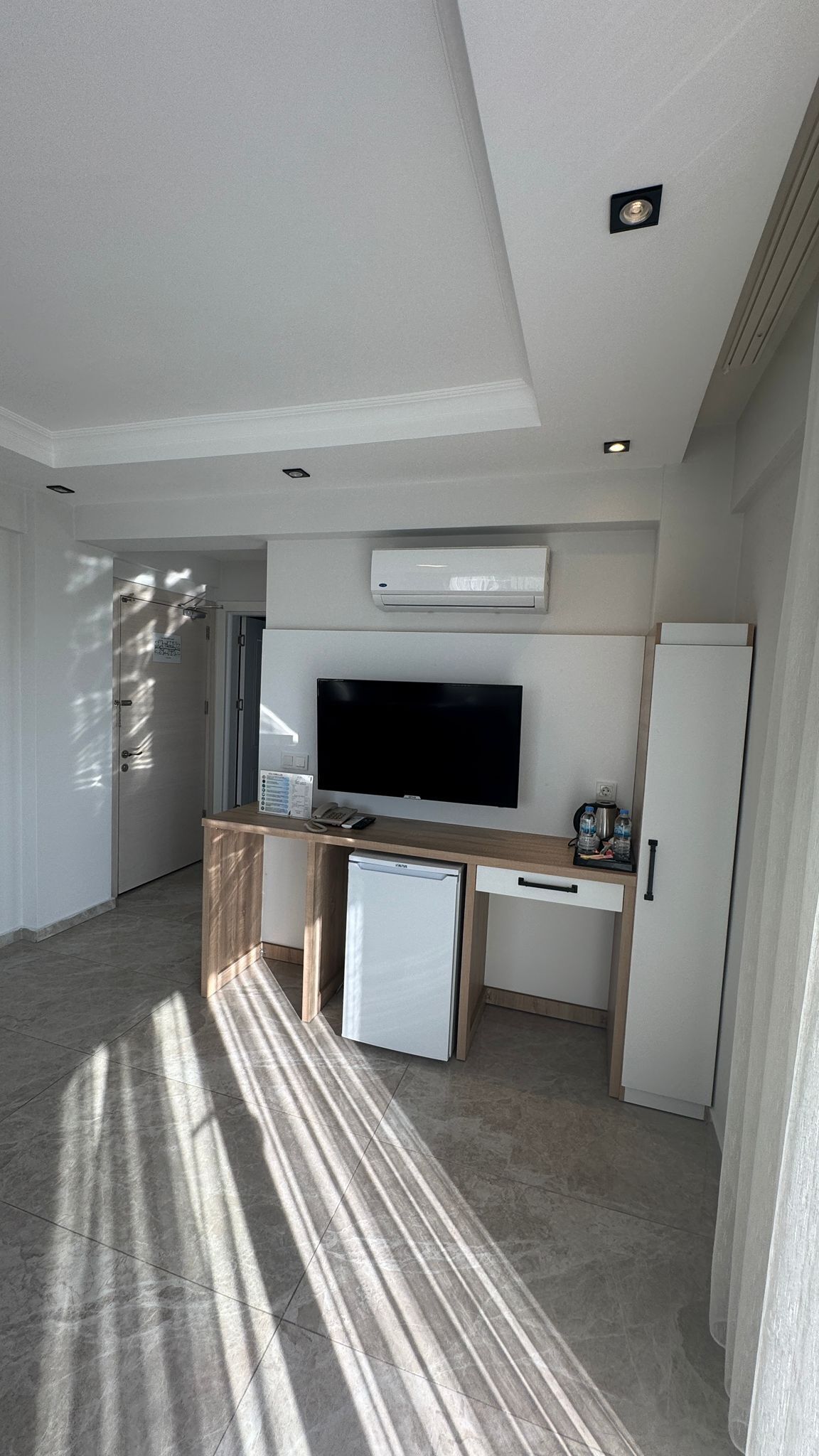 Una sala de estar moderna con televisor de pantalla plana, un refrigerador pequeño, una cafetera y un mueble bajo.