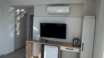 Una sala de estar moderna con televisor de pantalla plana, un refrigerador pequeño, una cafetera y un mueble bajo.