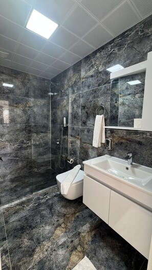 Un baño moderno con ducha envuelta en vidrio, un lavamanos blanco y un salpicadero de mármol.