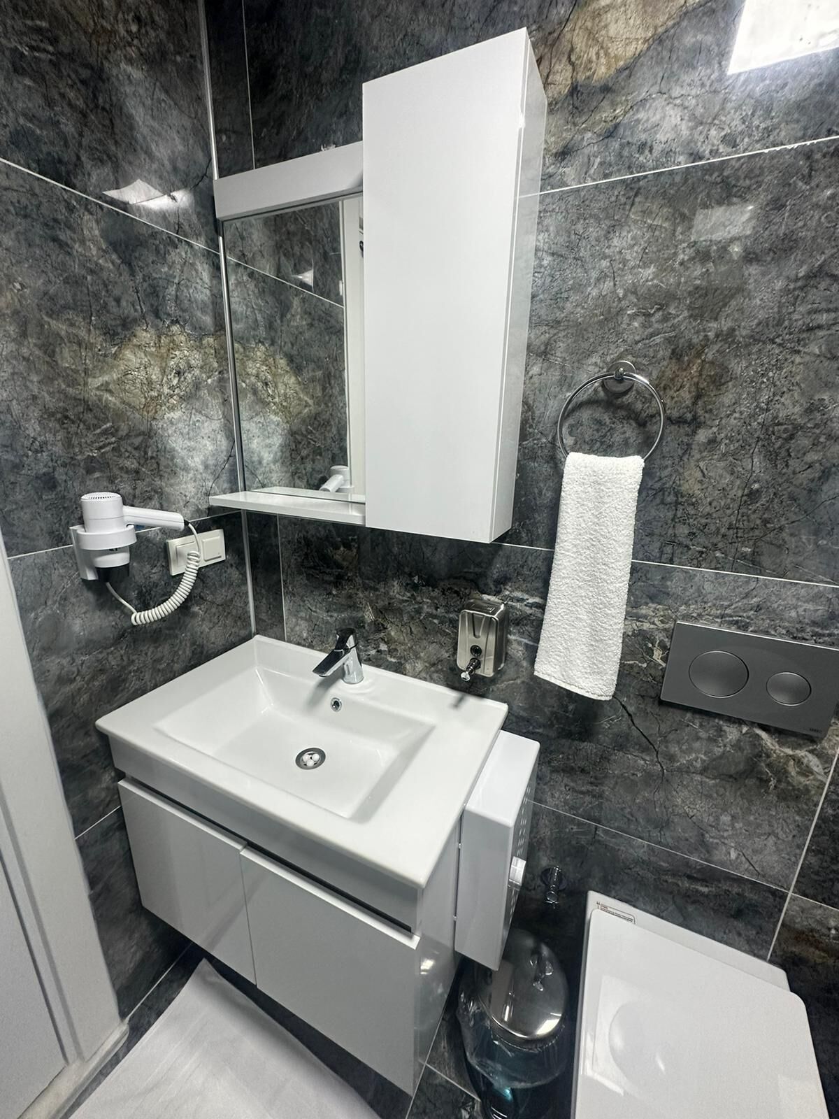 A modern bathroom with a white sink, a mirror, a towel rack, and a toilet.