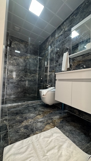A modern bathroom with a glass-enclosed shower, a white toilet, and a marble-tiled floor. - The Brothers Suite (Dalaman)