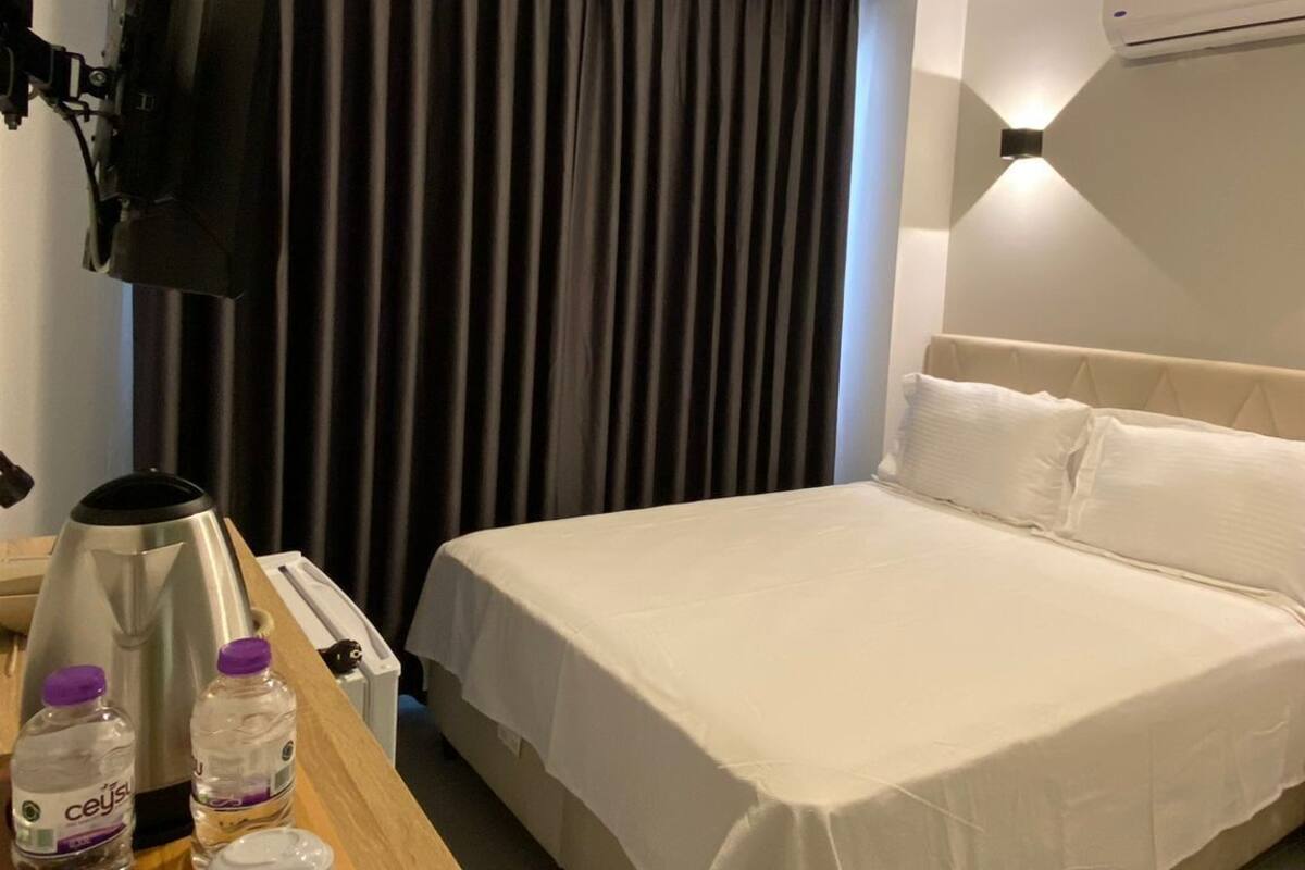 A hotel room with a bed, a desk with a tray of breakfast items, a flat-screen TV, and an air conditioning unit.