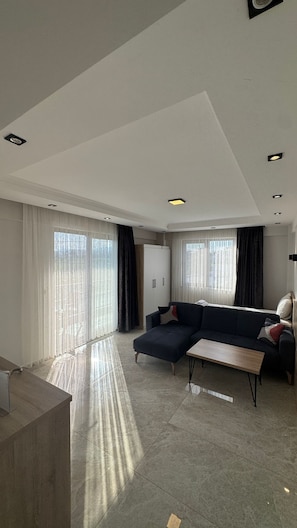 A spacious living area with a dark-colored sofa, a small wooden table, and a cabinet. - The Brothers Suite (Dalaman)