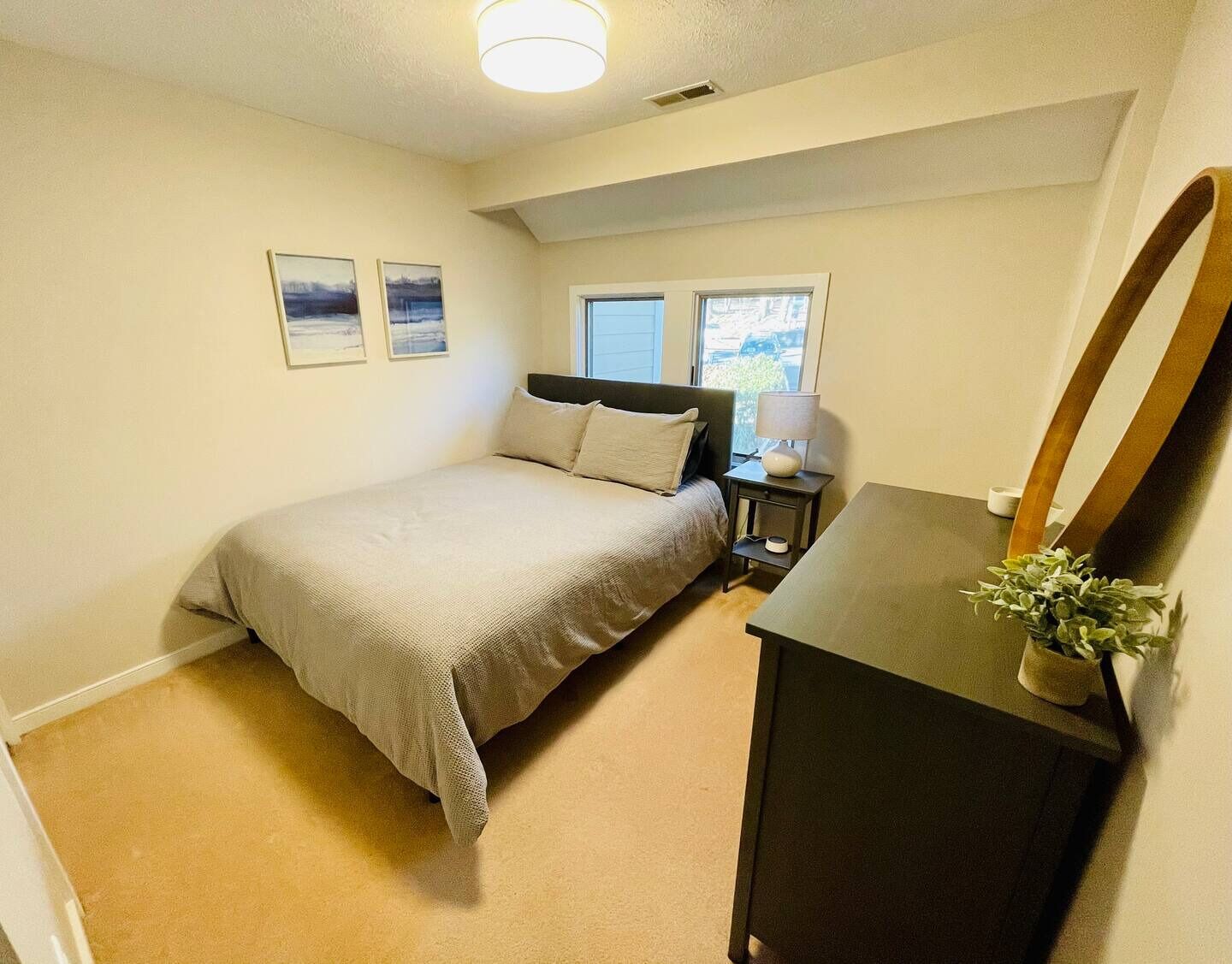 Une chambre à coucher comprenant un lit, une table de chevet, une lampe, un miroir et deux tableaux encadrés accrochés au mur.