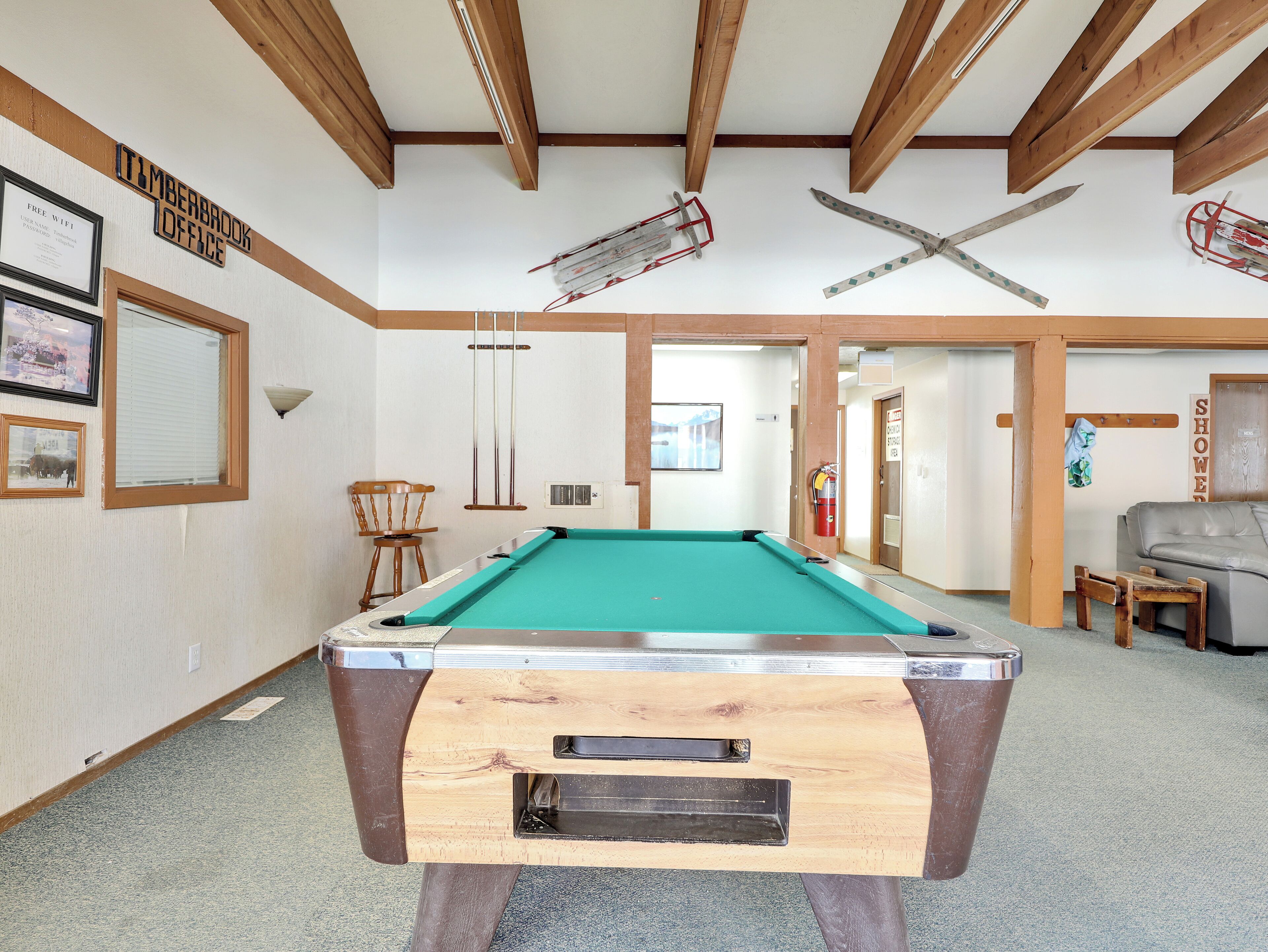 A pool table in a room with wooden beams on the ceiling, a chair, and a sofa.