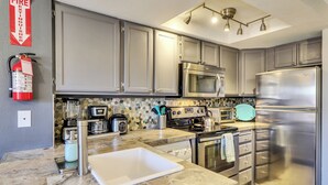 A modern kitchen with stainless steel appliances, a granite countertop, and a fire extinguisher mounted on the wall. - Mountain Retreat Close the Slopes (Brian Head)