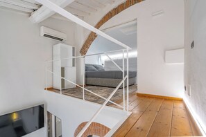 Ein modernes Schlafzimmer im Loft-Stil mit Holzboden, einem Bett, einer weißen Treppe und einem Fernseher.