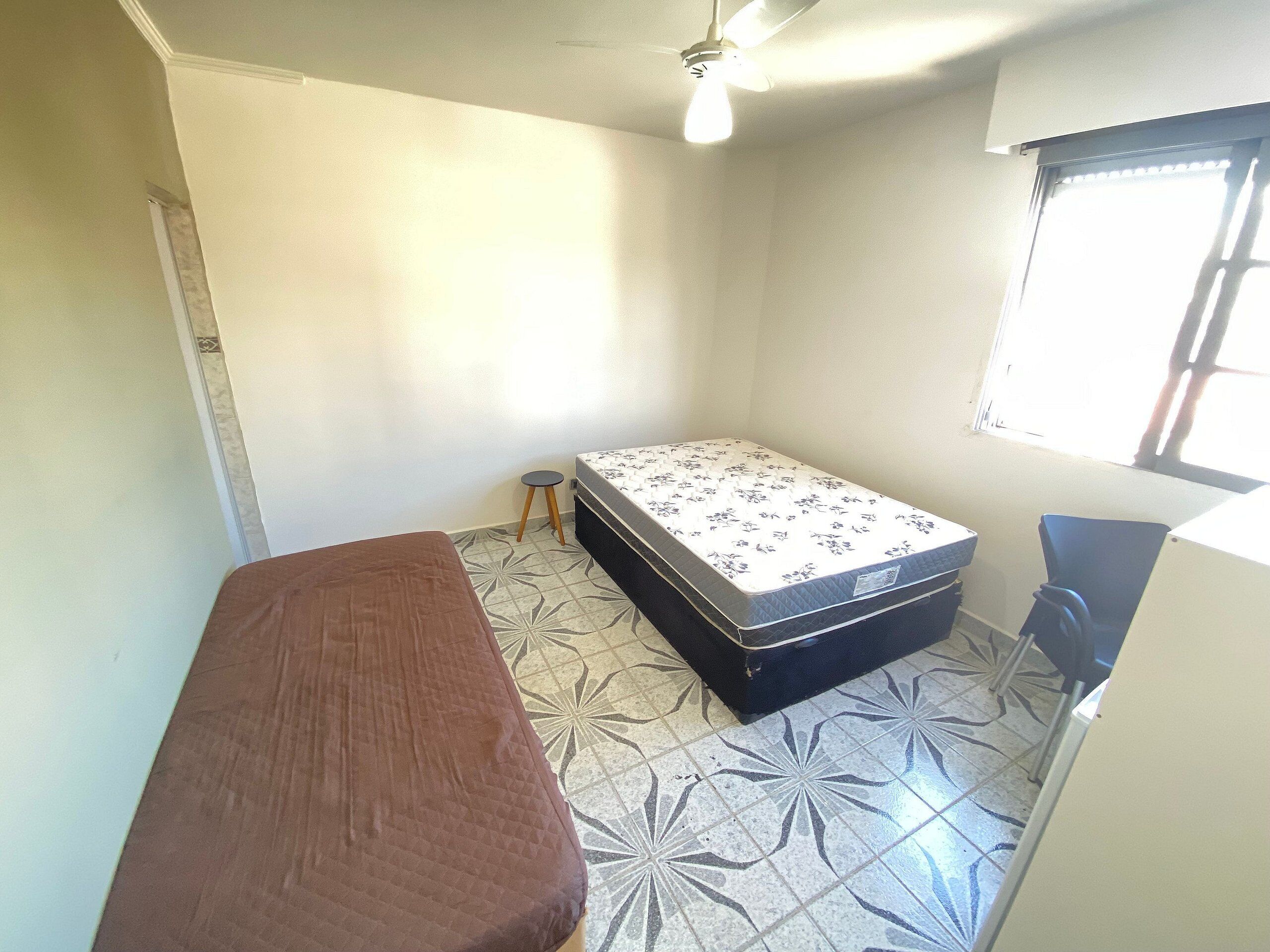 A small, sparsely furnished room with a single bed, a bench, and a window.