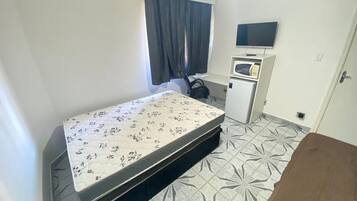 Una habitación pequeña y limpia con cama, escritorio, televisor y refrigerador.