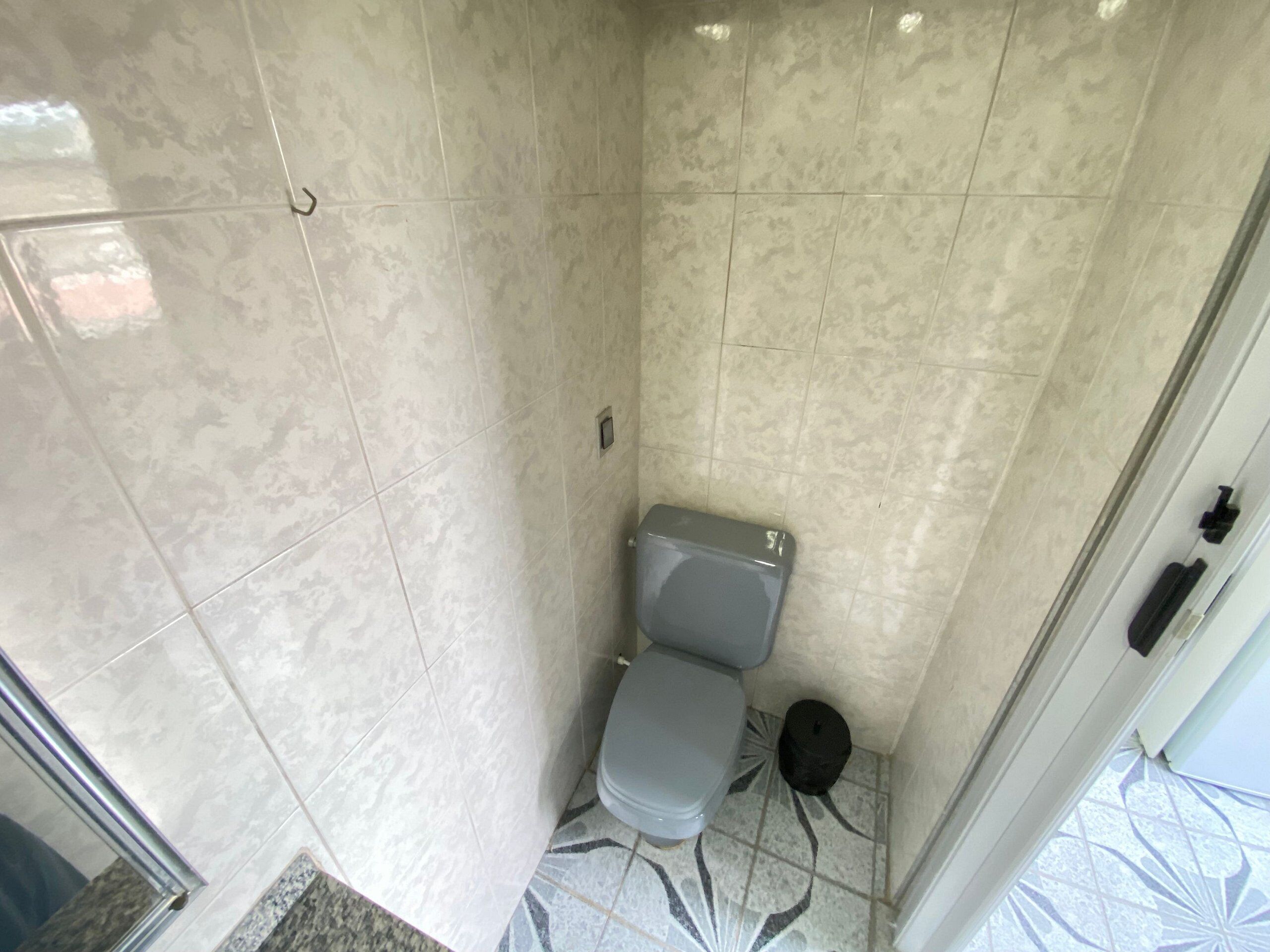 A bathroom with a toilet, a small trash bin, and a patterned floor.
