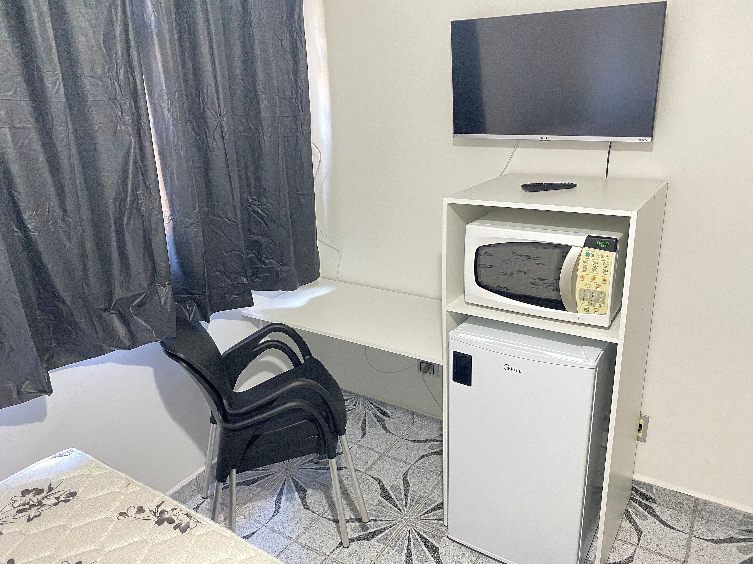 A compact room with a bed, a desk, a chair, a television, a microwave, and a refrigerator.