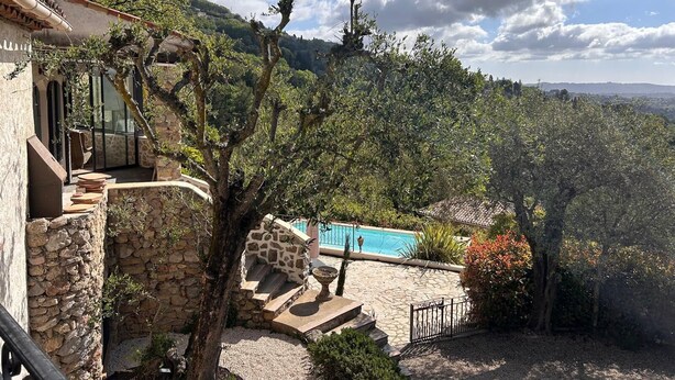 Un bâtiment en pierre doté d’une piscine, entouré d’arbres et de collines.