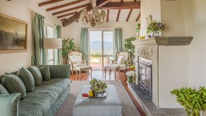 A cozy living room with a fireplace, green curtains, and a view of the outdoors. - Fairytale Farmhouse Villa with Views and Pool (Lucca)