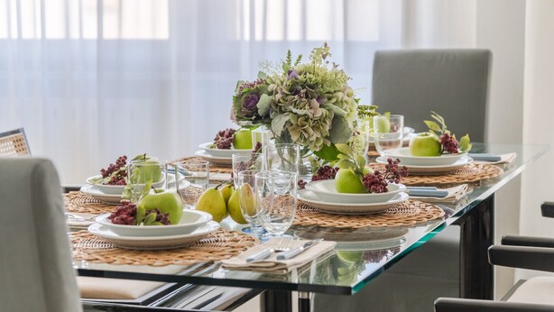 A dining table set with plates of green apples, glasses, and a centerpiece of flowers. - Experience  Beachfront Coastal Elegance at Ocean Breeze (Lido di Camaiore)
