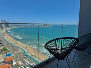Un balcón con vista a una playa y al océano, con dos sillas negras.