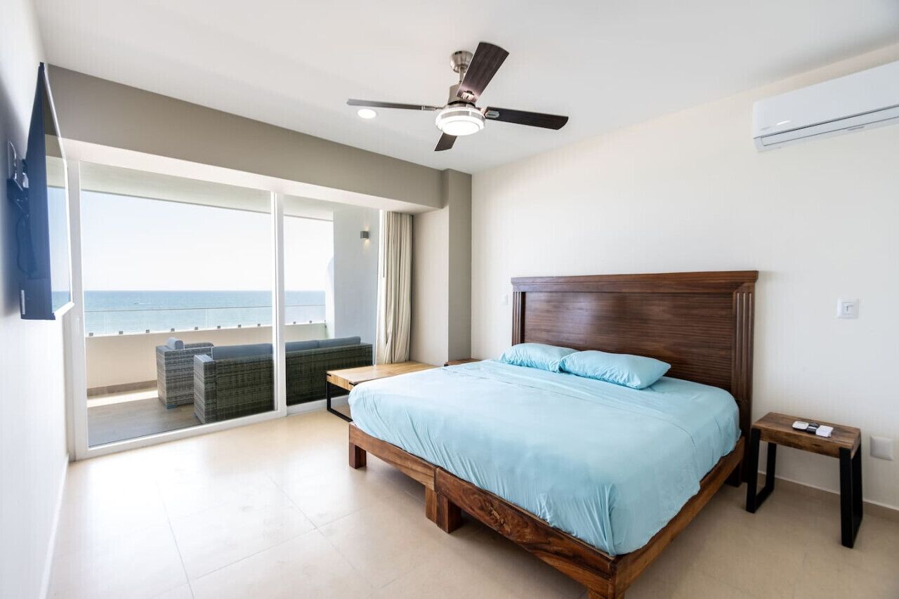 Un dormitorio con una cama grande, un ventilador de techo y vista al océano a través de una puerta corrediza de vidrio.