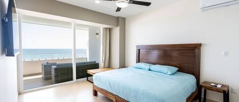Un dormitorio con una cama grande, un ventilador de techo y vista al océano a través de una puerta corrediza de vidrio.