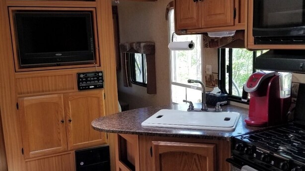 A compact RV kitchen with wooden cabinets, a built-in stove, a microwave, and a window for natural light. - The Riverside Dutchmen.  Reconnect with nature (Petit Étang)