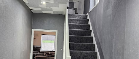 A staircase with carpeted steps leading to a landing. The walls are grey with a textured pattern.