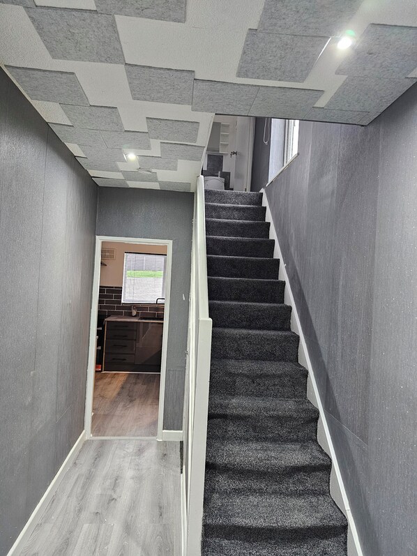 A staircase with carpeted steps leading to a landing. The walls are grey with a textured pattern.