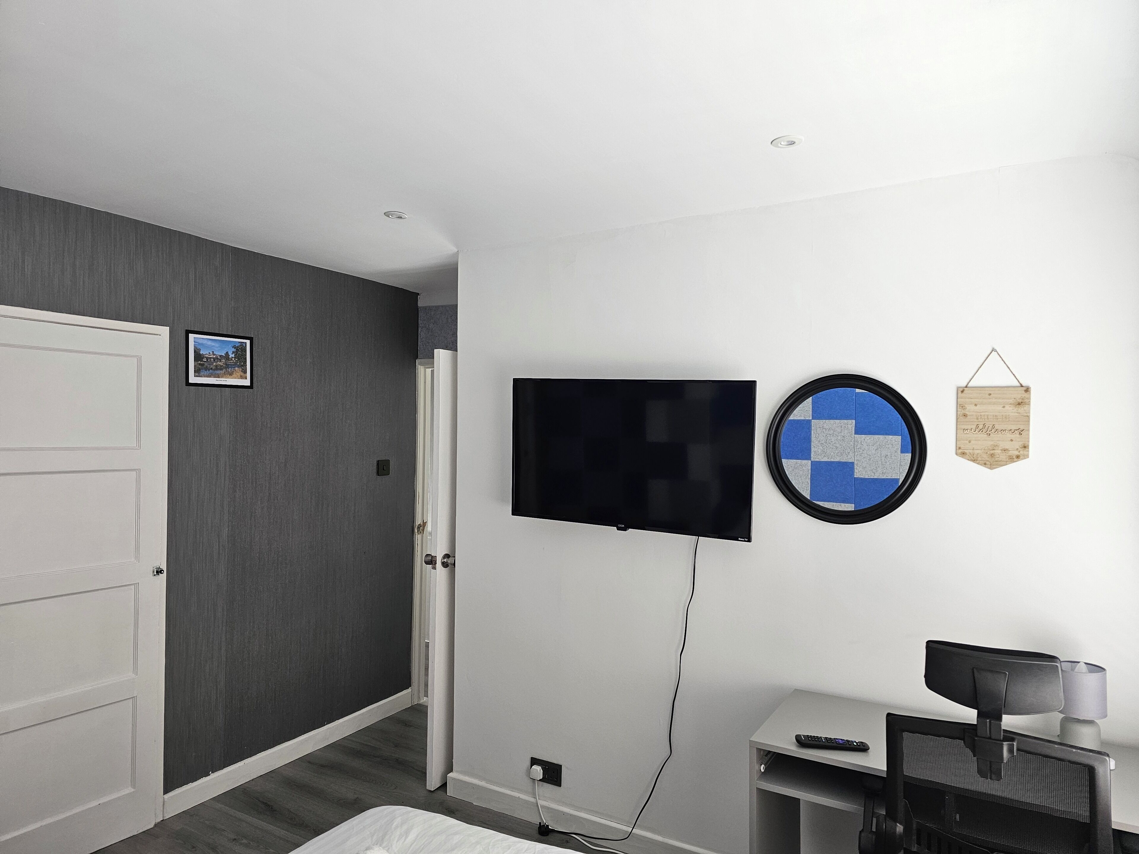 Ett hotellrum med en säng, ett skrivbord med en dator, en tv som är monterad på väggen och en dörr.