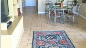 A hallway with a dining area, a TV, and a patterned rug.