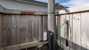 A metal showerhead attached to a wooden fence with a hose. - Cooks Family Retreat - Cooks Beach Holiday Home (Whitianga)