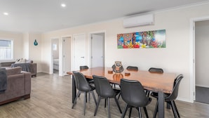 A modern living room with a wooden dining table, black chairs, a grey sofa, and a colorful abstract painting on the wall. - Cooks Family Retreat - Cooks Beach Holiday Home (Whitianga)