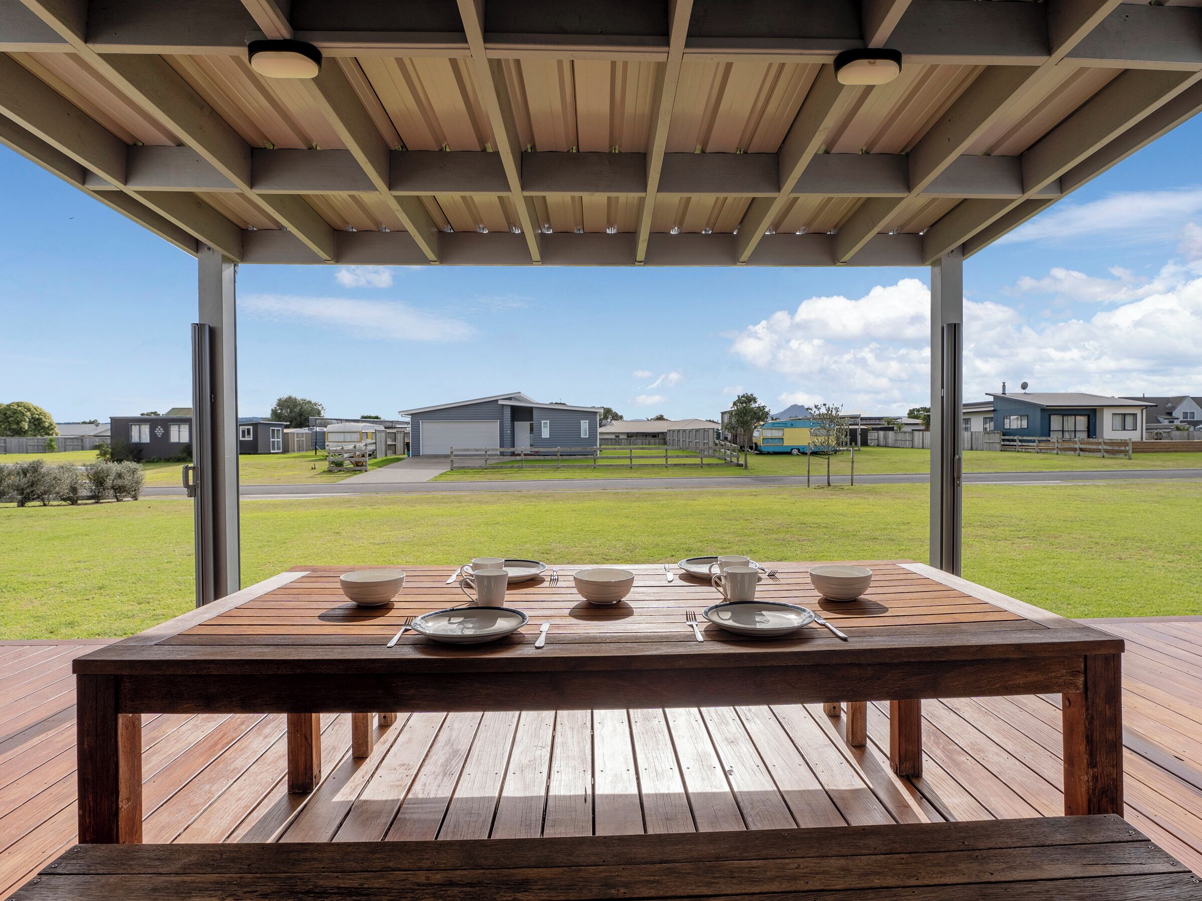 A wooden deck with a table set for dining, overlooking a residential area with houses and a road.