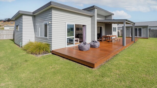 A modern single-story house with a wooden deck, large sliding glass doors, and a covered outdoor seating area. - Cooks Family Retreat - Cooks Beach Holiday Home (Whitianga)
