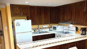 A kitchen with wooden cabinets, a white refrigerator, a stove, a microwave, and a tiled backsplash. There are three bar stools and a sink. - Marina Sol Resort Condo in Cabo
(Cabo San Lucas)