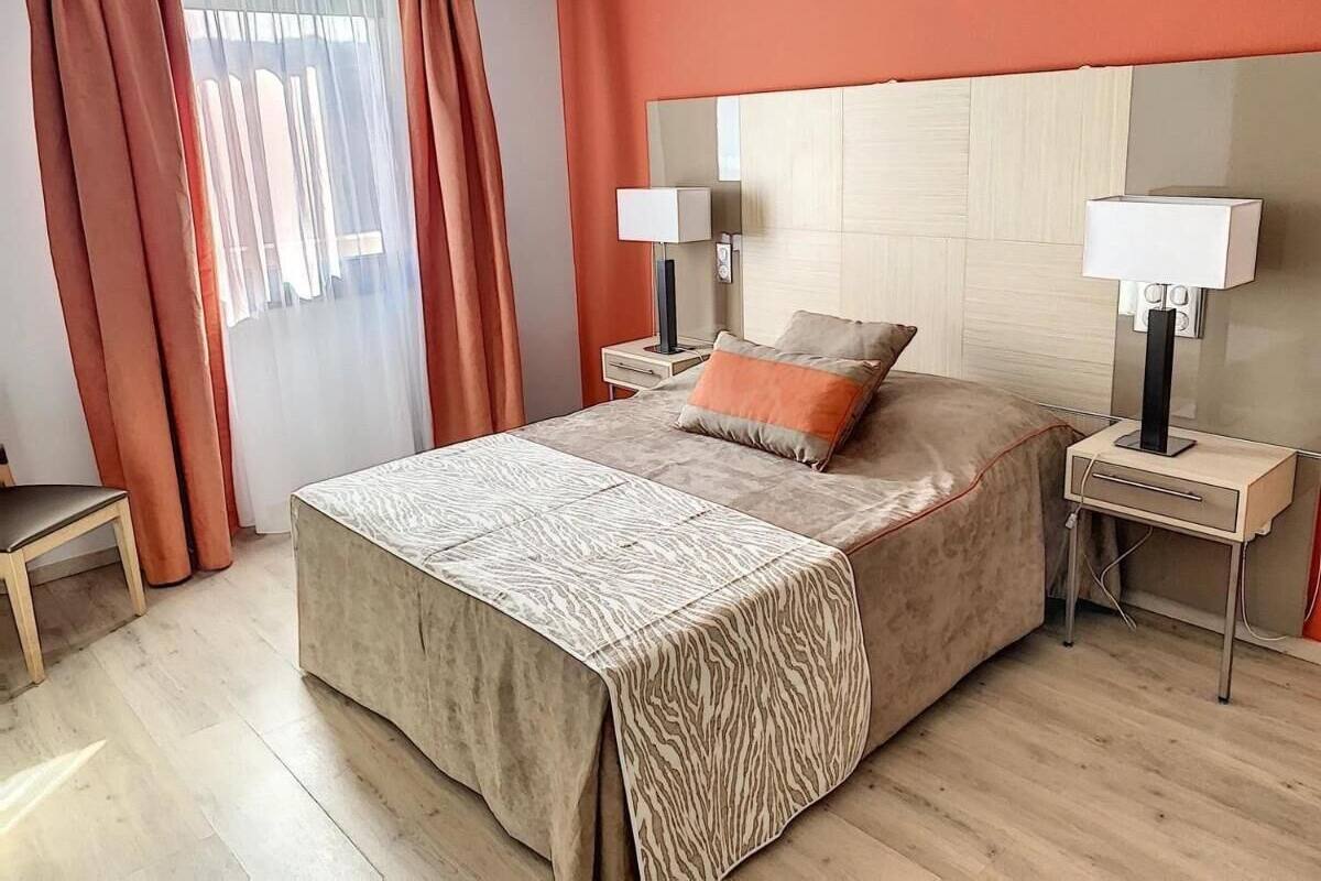 Une chambre à coucher comprenant un lit, deux tables de chevet, une commode et une fenêtre avec des rideaux.