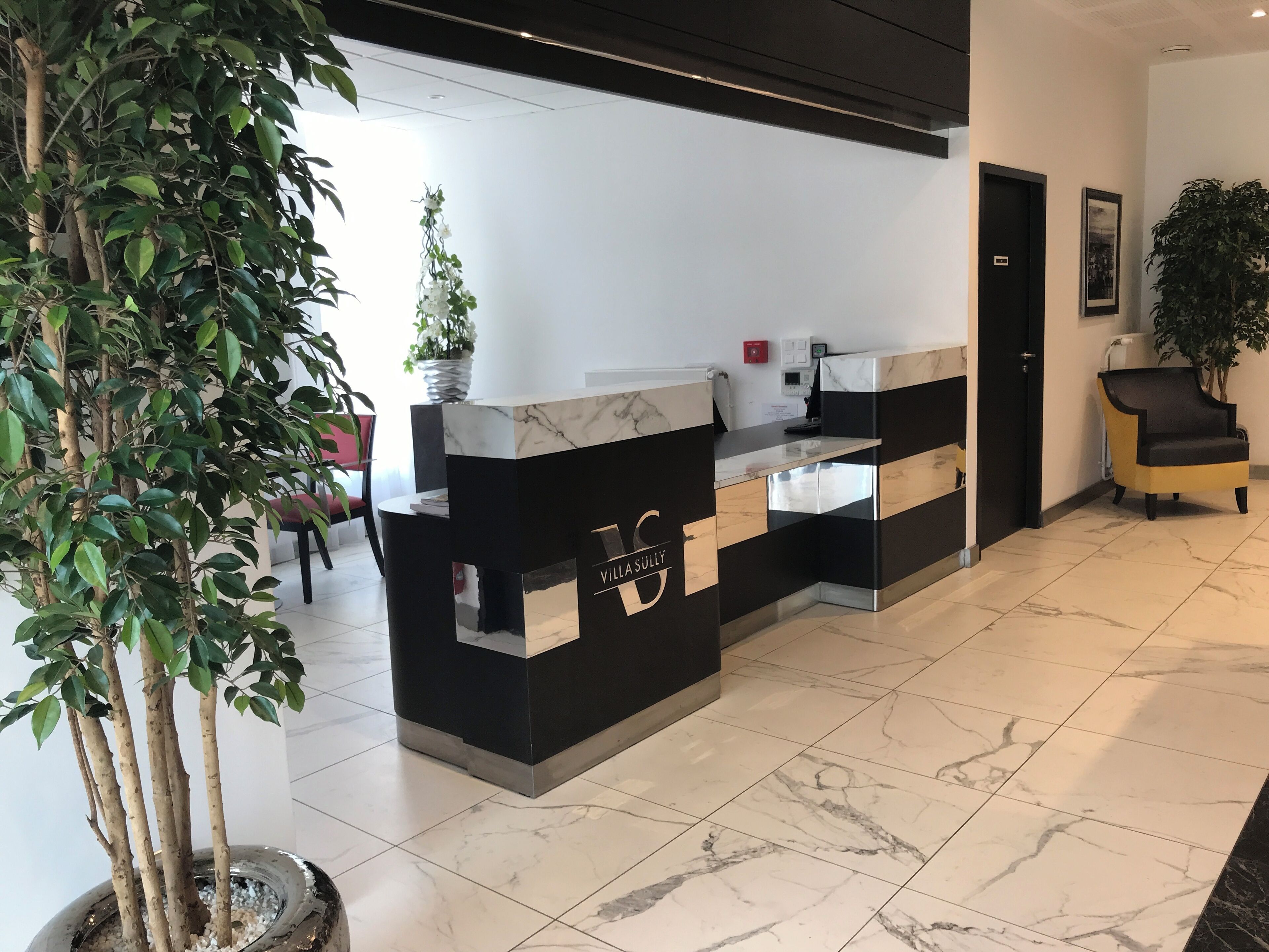 A reception desk with a marble top and black base, a potted plant to the left, and a chair to the right.