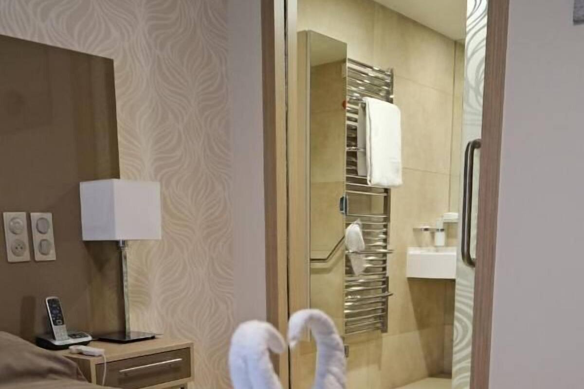 Une chambre d’hôtel avec un lit, une table de chevet avec une lampe et une salle de bain visible à travers une porte ouverte.