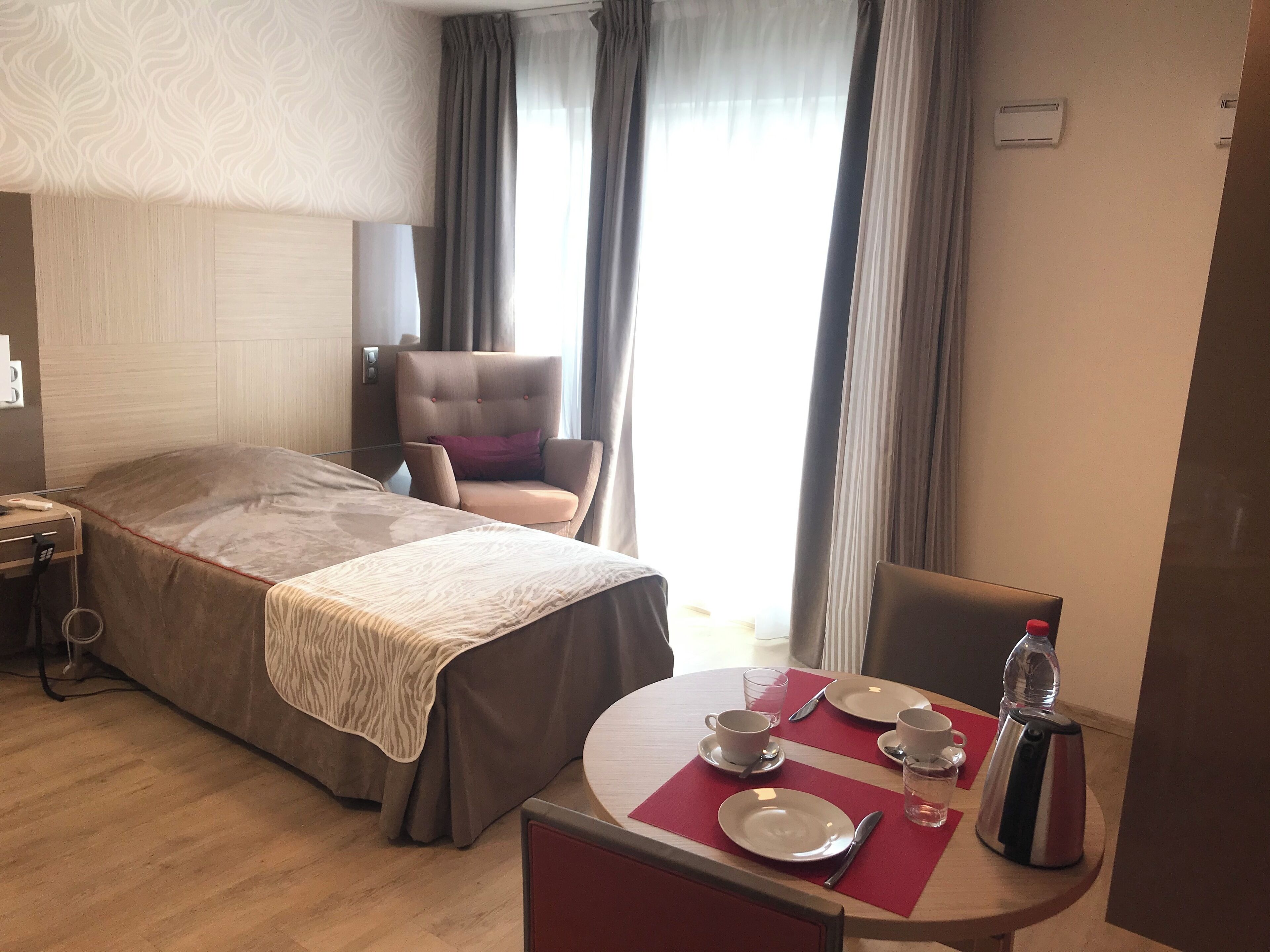 Habitación de hotel con cama, una silla, una mesa de comedor, platos, tazas y una tetera.