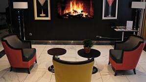 A lobby with a fireplace, two armchairs, a small table, and a potted plant. - Appart One Montreuil - Croix de Chavaux (Montreuil)