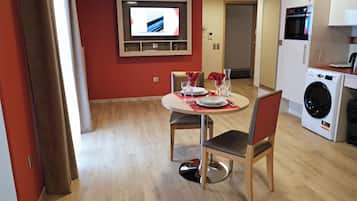 A dining area with a table set for two, a TV mounted on the wall, and a washing machine in the background.