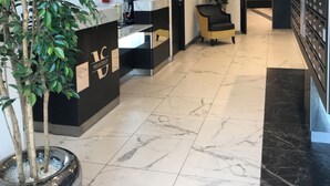 A modern reception area with a marble floor, a reception desk, a potted plant, and a wall-mounted digital display. - Appart One Montreuil - Croix de Chavaux (Montreuil)