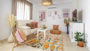 A living room with a sofa, coffee table, and decorative pillows. There is a television, a potted plant, and a rug.