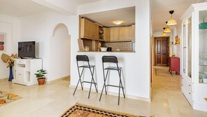 A modern kitchen with two bar stools, a television, and a potted plant.