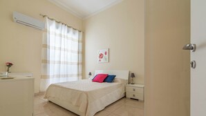 A bedroom with a bed, bedside tables, an air conditioning unit, a desk, and a window with curtains. - Olivella Apartment al Teatro Massimo by Wonderful Italy (Palermo)