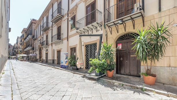 A cobblestone street lined with multi-story buildings, some with balconies and potted plants. - Olivella Apartment al Teatro Massimo by Wonderful Italy (Palermo)