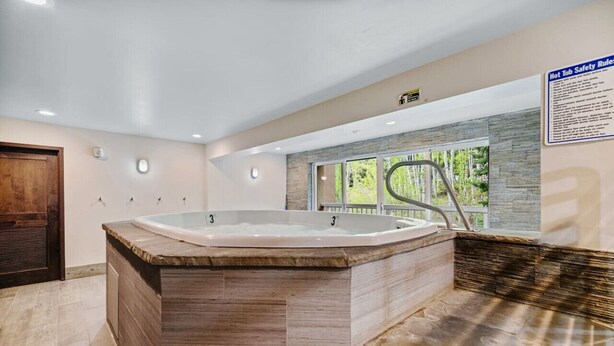 Ein Wellnessbereich mit einer großen Whirlwanne, einer Holzbank und einem Fenster mit Blick auf Bäume.