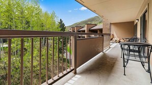 Ein Balkon mit Blick auf Bäume und einen Berg, eine überdachte Terrasse sowie Gartenmöbel.