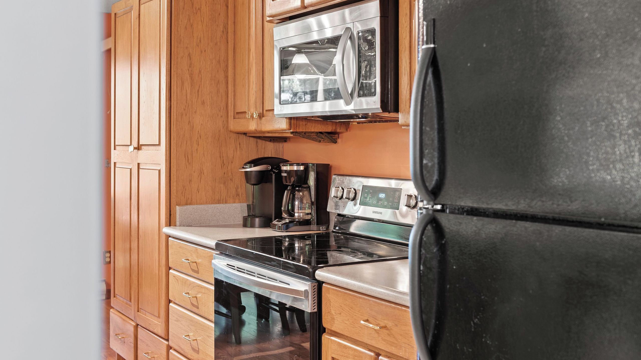 A kitchen with wooden cabinets, a stainless steel refrigerator, a microwave, a coffee maker, and an oven.