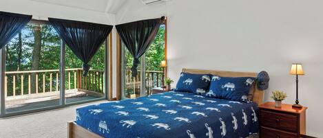 A bedroom with a bed, nightstand, lamp, and large windows with curtains.