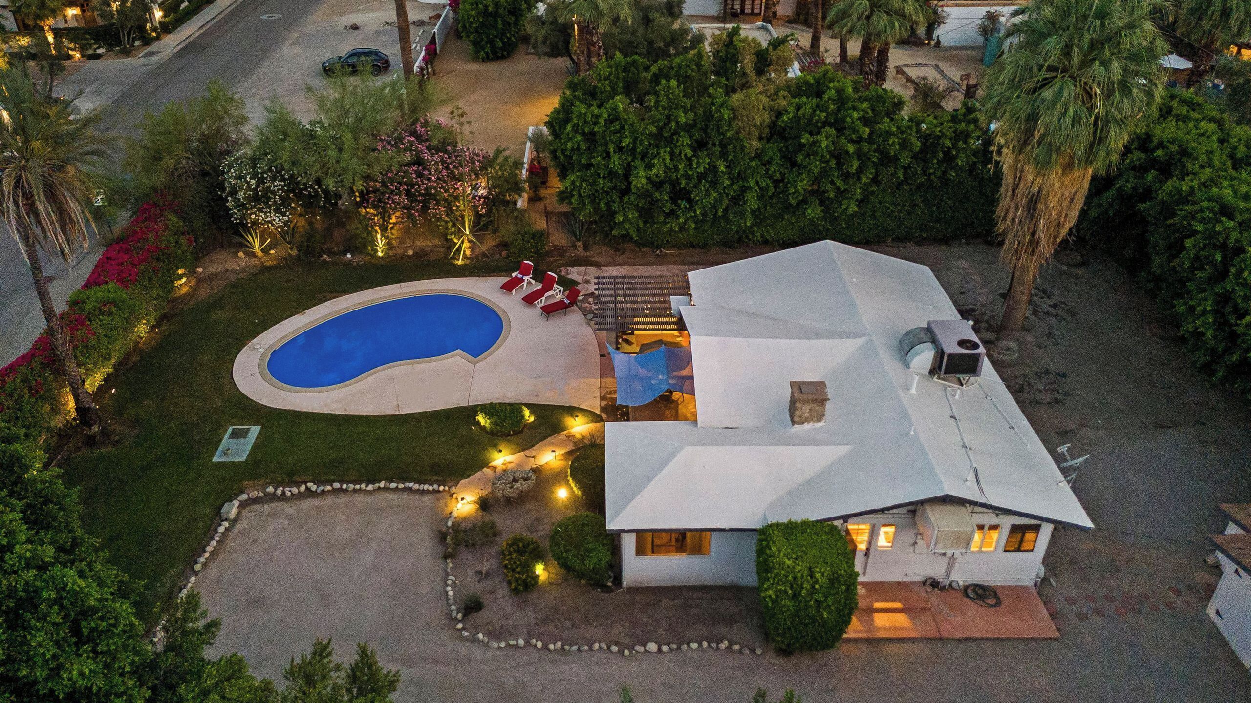 A house with a swimming pool, a patio with chairs, and a well-maintained lawn.