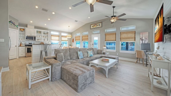 A spacious living area with a large sectional sofa, a dining table, and a kitchen with white cabinetry. - Steps to Beach, Balcony, Ocean View Golf Cart Zone Casa Rosada by Avantstay (Port Aransas)
